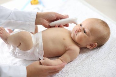 Pediyatrist bebeğin sıcaklığını hastanede termometreyle ölçüyor.
