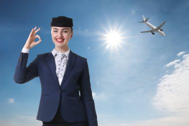 Üniformalı mutlu hostes mavi gökyüzüne uçakla işaret veriyor.