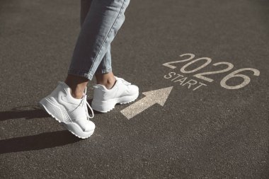 Yeni yıl 2026. Kadın kelime ile asfalt üzerinde yürüyor Başla, ok ve sayılar, yakın plan
