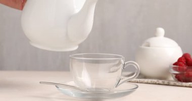 Beyaz masada çaydanlıktan fincana çay dolduran kadın, yakın plan.