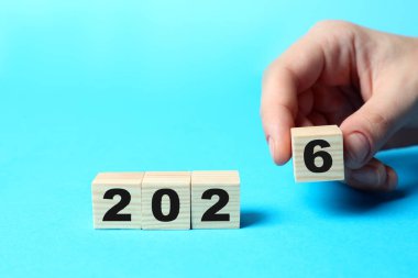 Yeni yıl 2026. Açık mavi arkaplanda 6 numaralı küpü diğerlerinin yanına koyan kadın, yakın plan.