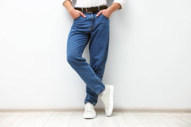 Beyaz duvarın yanında şık kotlu adam, yakın plan.