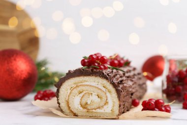 Lezzetli Noel kütüğü (geleneksel Noel pastası) kırmızı frenk üzümü ve beyaz masada bulanık ışıklara karşı dekor ile yakın plan. Bokeh etkisi