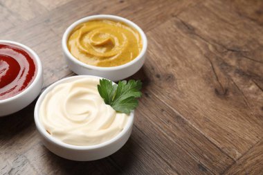 Tabaklardaki farklı lezzetli soslar ve ahşap masada maydanoz, yakın plan. Metin için boşluk