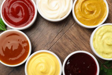 Tabaklardaki farklı lezzetli soslardan yapılmış çerçeve ve ahşap masadaki maydanozdan yapılmış, düz bir döşeme. Metin için boşluk