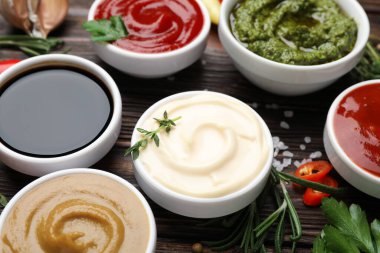 Farklı soslar, baharatlar ve otlar ahşap masada, yakın plan.