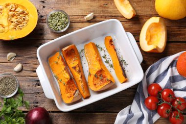 Baked pumpkin and ingredients on wooden table, flat lay