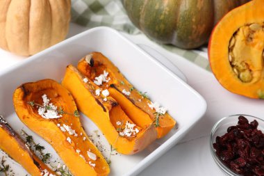 Beyaz ahşap masada fırınlanmış balkabağı ve malzemeler, yakın plan.