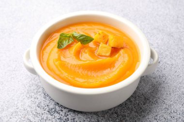 Gri masada servis edilen fesleğenli balkabağı kremalı çorba, yakın plan.