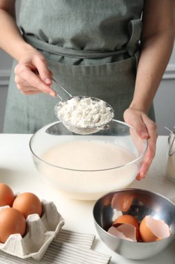 Hamur yapmak (sıvı hamur). Beyaz masada un yiyen bir kadın. Kapalı alanda, yakın plan.