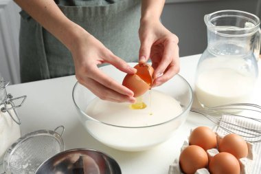 Hamur yapmak (sıvı hamur). Beyaz masadaki kaseye yumurta ekleyen kadın, yakın plan.