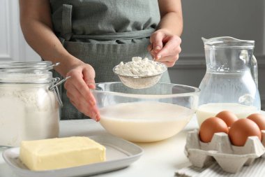 Hamur yapmak (sıvı hamur). Beyaz masada un yiyen bir kadın. Kapalı alanda, yakın plan.