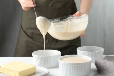 Kadın hamur hamurunu (sıvı hamur) içerideki masada yemek tabaklarına döküyor, yakın plan.