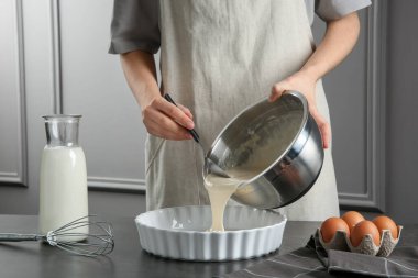 Mutfaktaki gri masada kaseden yemek kabına sıvı hamur döken kadın, yakın plan.