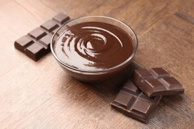 Erimiş çikolata ve parçalarla dolu bir kase, ahşap masa, yakın plan.