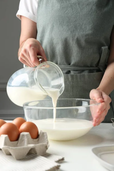 Hamur yapmak (sıvı hamur). Beyaz masadaki kaseye süt döken kadın, yakın plan.