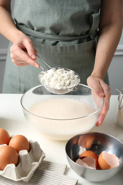 Hamur yapmak (sıvı hamur). Beyaz masada un yiyen bir kadın. Kapalı alanda, yakın plan.