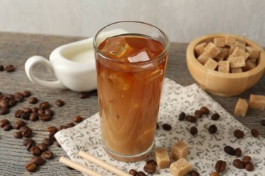 Lezzetli buzlu kahve bardakta süt, fasulye ve şeker küpleri ahşap masada gri arka planda, yakın plan