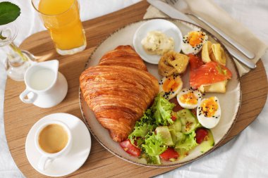 Tray with delicious breakfast on bed in hotel room, above view