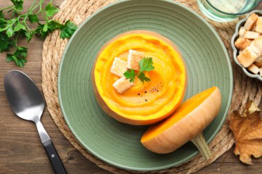 Maydanozlu balkabağı kremalı çorba ve ahşap masada balkabağı ile servis edilen kızarmış ekmek.