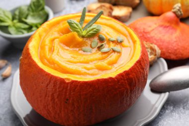 Çekirdekli ve fesleğenli balkabağı kremalı çorba. Gri masada servis edilmiş, yakın plan.