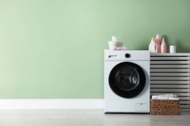 Çamaşır makinesi, deterjanlar ve temiz çamaşır sepeti. Kapalı alandaki yeşil duvarın yanında. Metin için boşluk