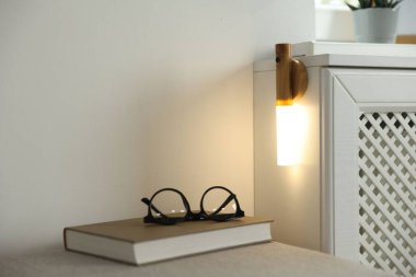 Puf gözlüklü ve evdeki duvarda taşınabilir LED lambalı bir kitap. Metin için boşluk