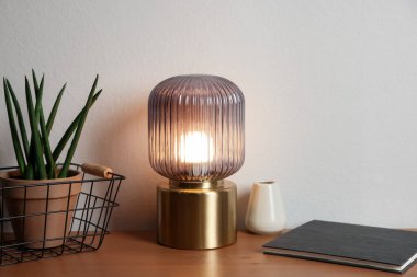 Şık lamba, vazo, çiçek ve kitap beyaz duvarın yanındaki ahşap masada.