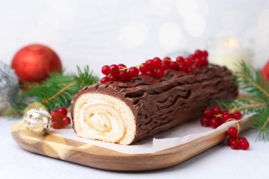 Lezzetli Noel kütüğü (geleneksel Noel pastası) kırmızı frenk üzümü, dekor ve köknar ağacı dallarıyla ışık masasında, yakın plan