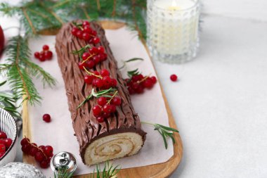 Lezzetli Noel kütüğü (geleneksel Noel pastası) kırmızı frenk üzümü ve köknar ağacı dalları ışık masasında, yakın plan