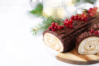 Lezzetli Noel kütüğü (geleneksel Noel pastası) kırmızı frenk üzümü, mum ve köknar ağacı dallarıyla beyaz fayanslı masa üzerinde, yakın plan. Metin için boşluk