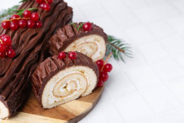 Lezzetli Noel kütüğü (geleneksel Noel pastası) beyaz fayanslı masa üzerinde kırmızı frenk üzümü, yakın plan. Metin için boşluk