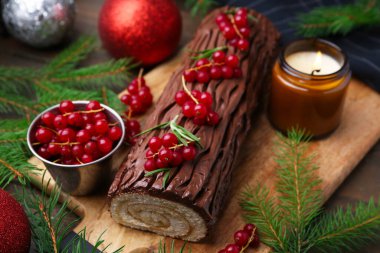 Lezzetli Noel kütüğü (geleneksel Noel pastası) kırmızı frenk üzümü, dekor ve köknar ağacı dalları ile masada, yakın plan