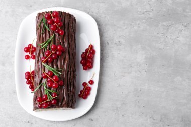 Lezzetli Noel kütüğü (geleneksel Noel pastası) gri desenli masa üzerinde kırmızı frenk üzümü, üst manzara. Metin için boşluk