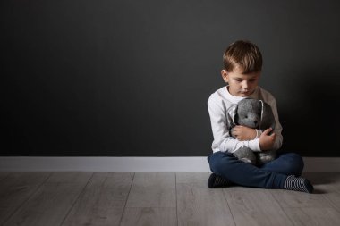 Siyah duvarın yanında oyuncak tavşancığı olan üzgün küçük bir çocuk.