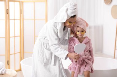 Anne ve kız göz bantlı ve banyoda bornoz giyen saçları sarılı.