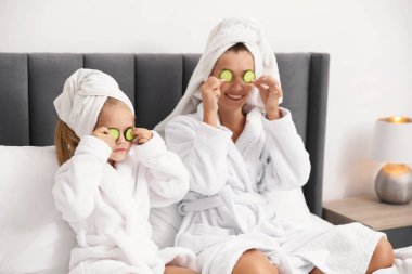 Havlu ve salatalık dilimli bornozlu bir anne ve kız evde yataktalar.