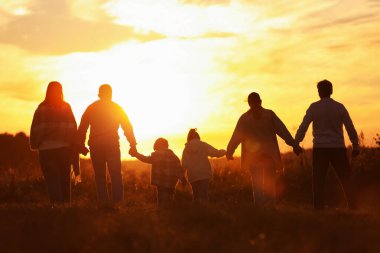 Aile gün batımında, arka planda el ele tutuşuyor.