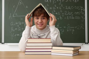 Okula dönelim. Ahşap masada kitap ve kırtasiye malzemesi olan öğrenci içeride matematik ödevi olan karatahtaya karşı.