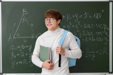 Okula dönelim. Sırt çantalı ve karatahtanın yanında matematik ödevi olan bir öğrenci.