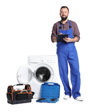 Beyaz arka planda bozuk çamaşır makinesinin yanında panosu olan profesyonel bir tamirci.