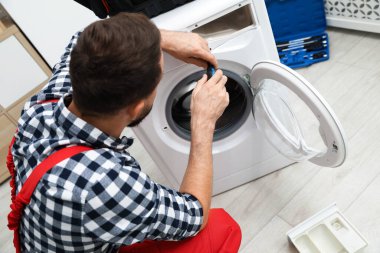 Profesyonel tamirci içeride bozuk çamaşır makinesini tamir ediyor.