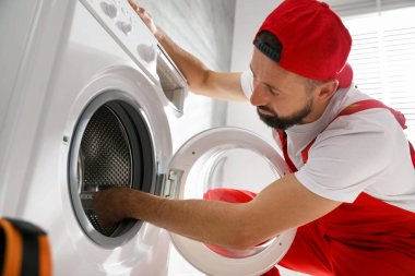 Profesyonel tamirci, bozuk çamaşır makinesini içeride tamir ediyor. Düşük açılı görüntü.