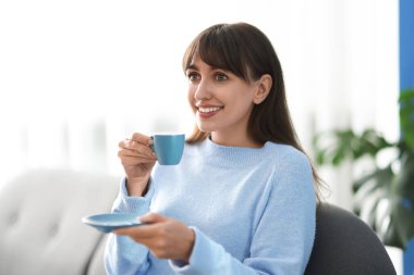 Evdeki kanepede kahve molası veren gülümseyen kadın.