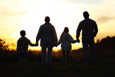 Aile gün batımında, arka planda el ele tutuşuyor.