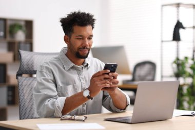 Ofisteki masada akıllı telefon kullanan adam.