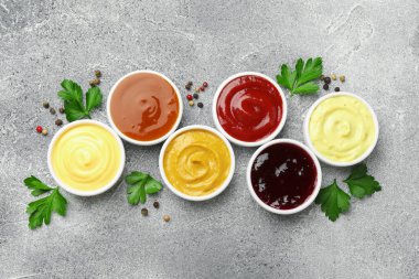Farklı lezzetli soslar kaselerde, maydanozlar ve biberler gri masada, düz yerde.
