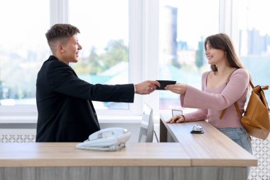 Resepsiyonist içeride misafir için pasaport veriyor.