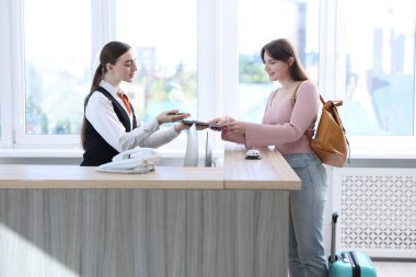 İçerideki resepsiyonda misafir ile çalışan resepsiyonist.