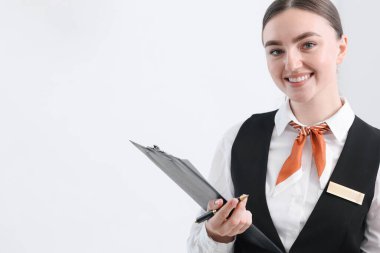 Beyaz duvarın yanında panosu ve kalemi olan mutlu bir resepsiyonist.